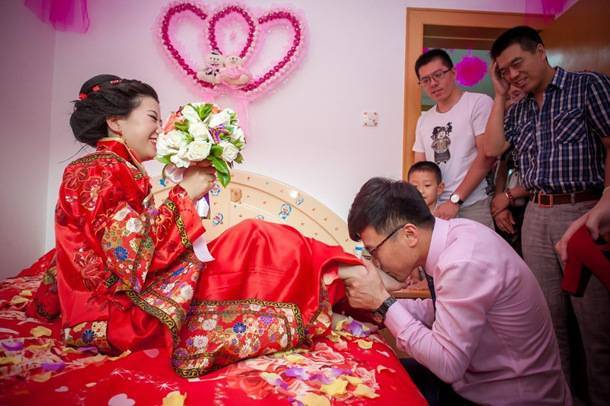 婚房里,新郎被亲友要求吻新娘的脚,新娘拿着捧花幸福而又害羞的笑着.