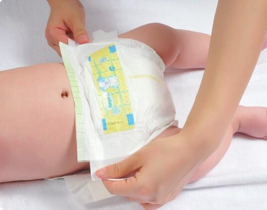 将尿布展开,一手提起宝宝的双脚,使宝宝屁股抬起,另一只手将新的纸